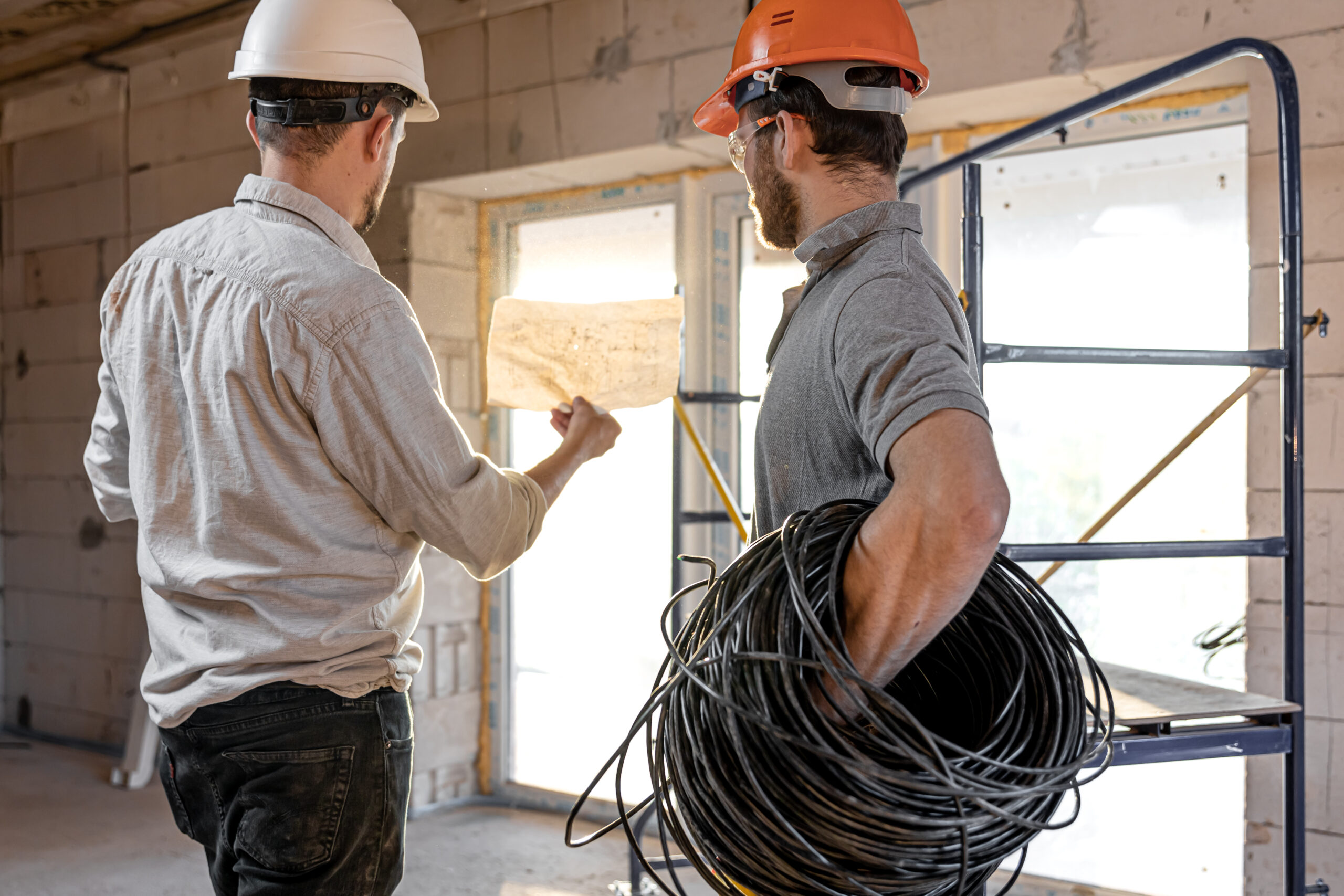 White card requirements for electricians - Two builder engineers talking at building site, engineer explaining a drawing to a worker.