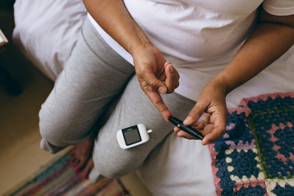 Testing blood sugar levels - Low section of mixed race female senior patient checking blood sugar level with glucometer at retirement home