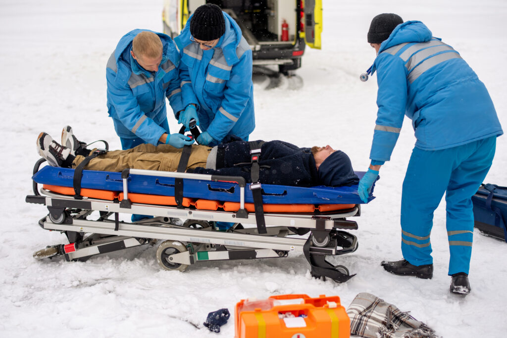 Two young paramedics in workwear fixing unconscious man with belts on stretcher
