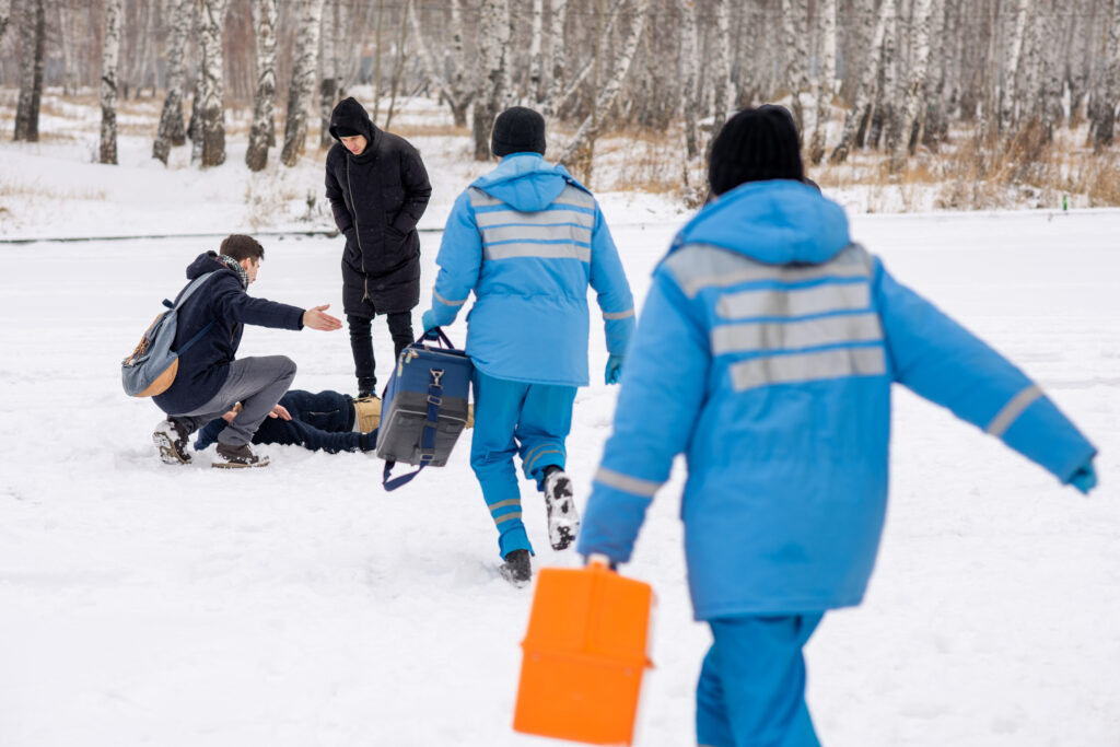 Rear view of paramedics in blue uniform hurrying to sick person lying in snow