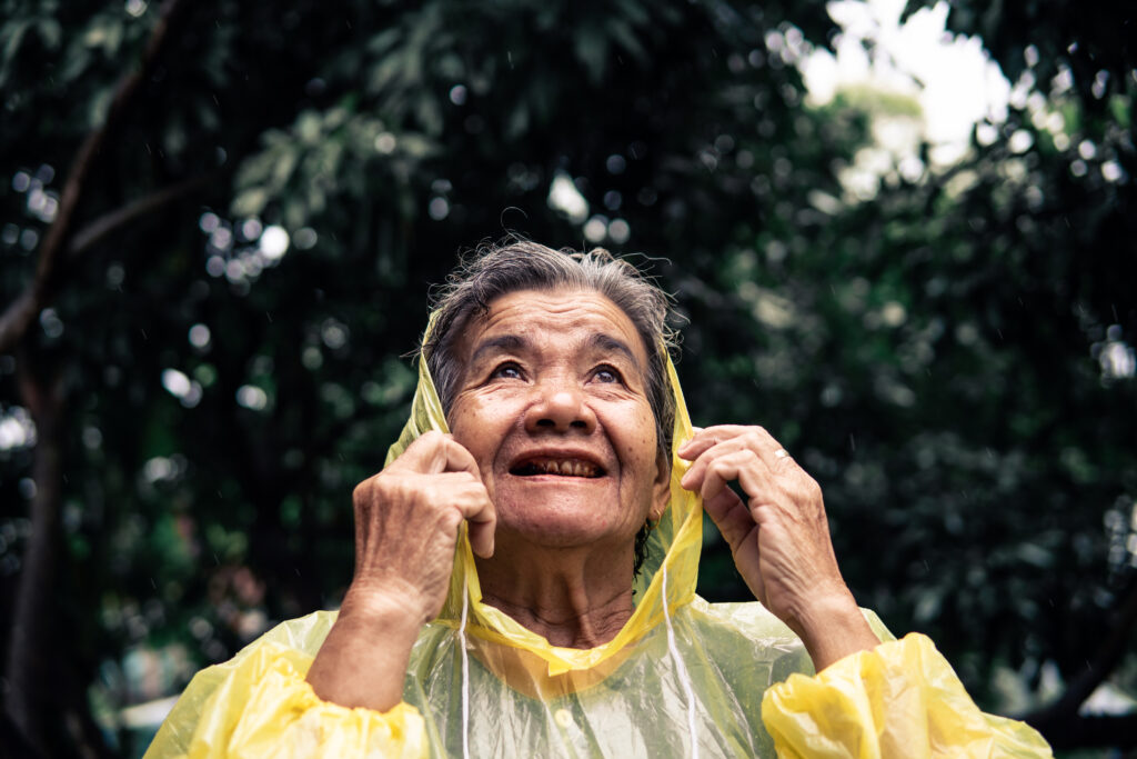 senior-woman-smiling-in-the-rain-wearing-yellow-raincoat.