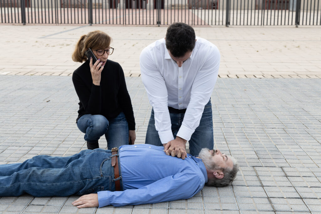 Passers helping an unconscious man outdoors - first aid concept